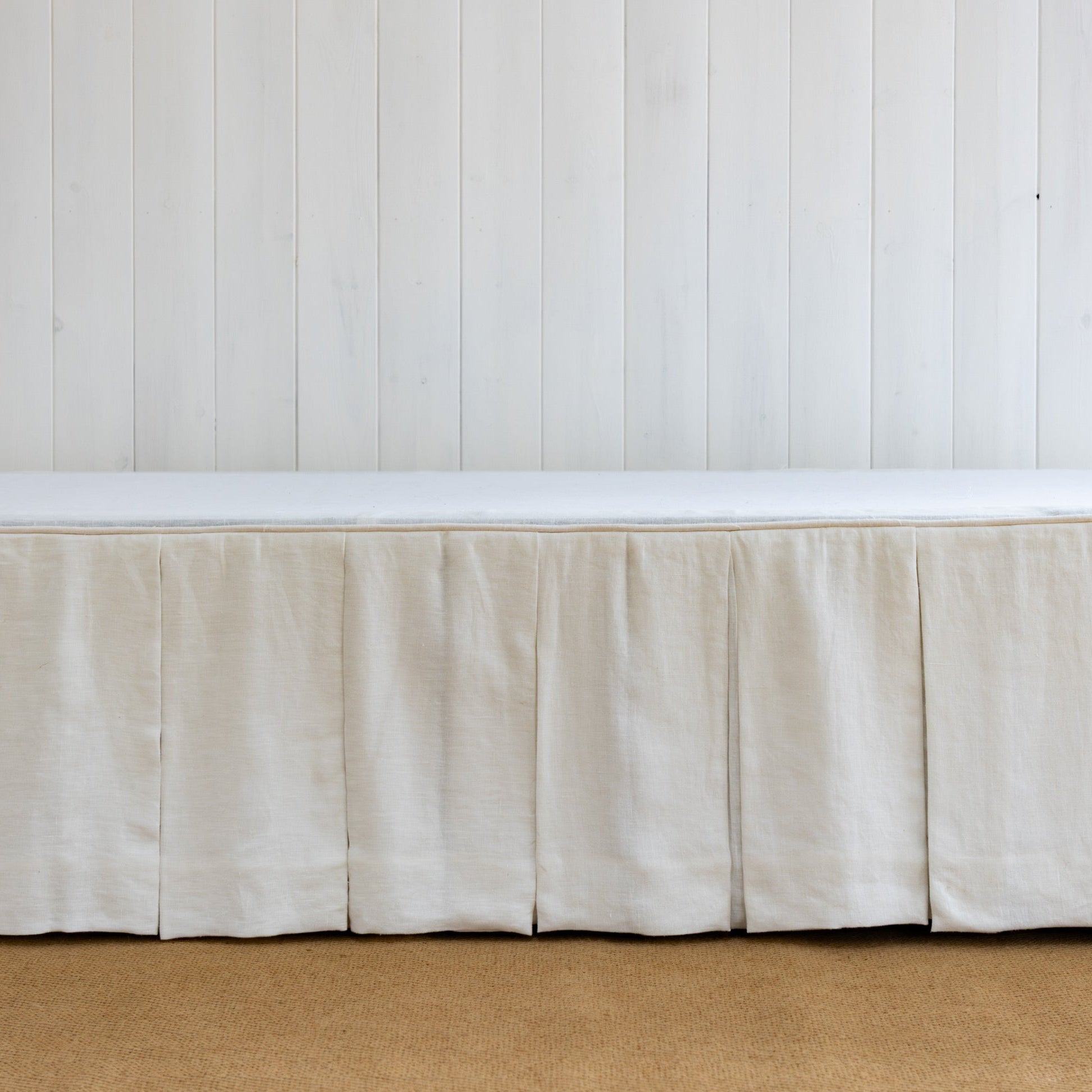 White bed skirt on a bed against a white paneled wall.