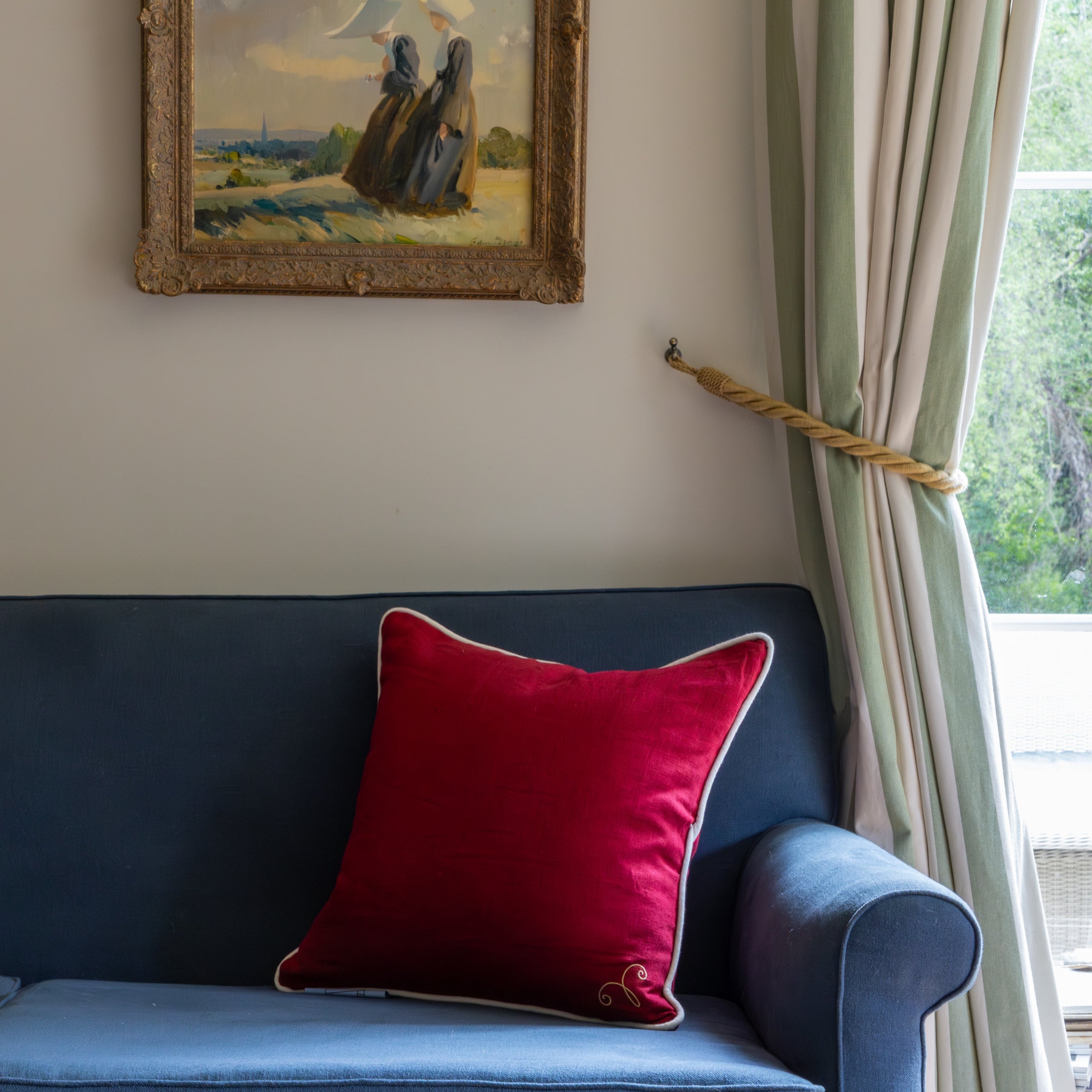 Blue sofa with a red pillow, framed painting on the wall, and green curtains.