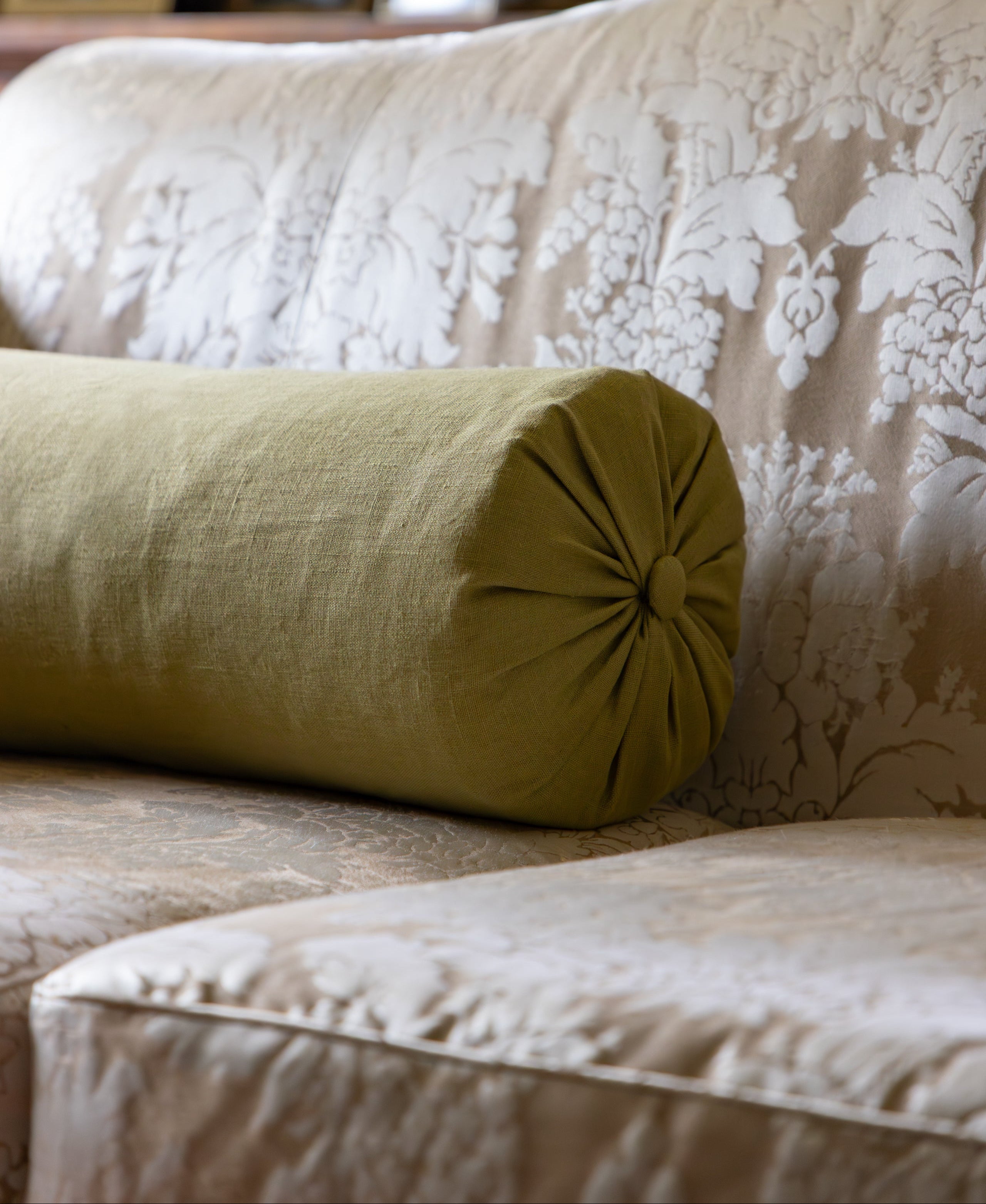 Green cylindrical pillow on a beige floral-patterned sofa