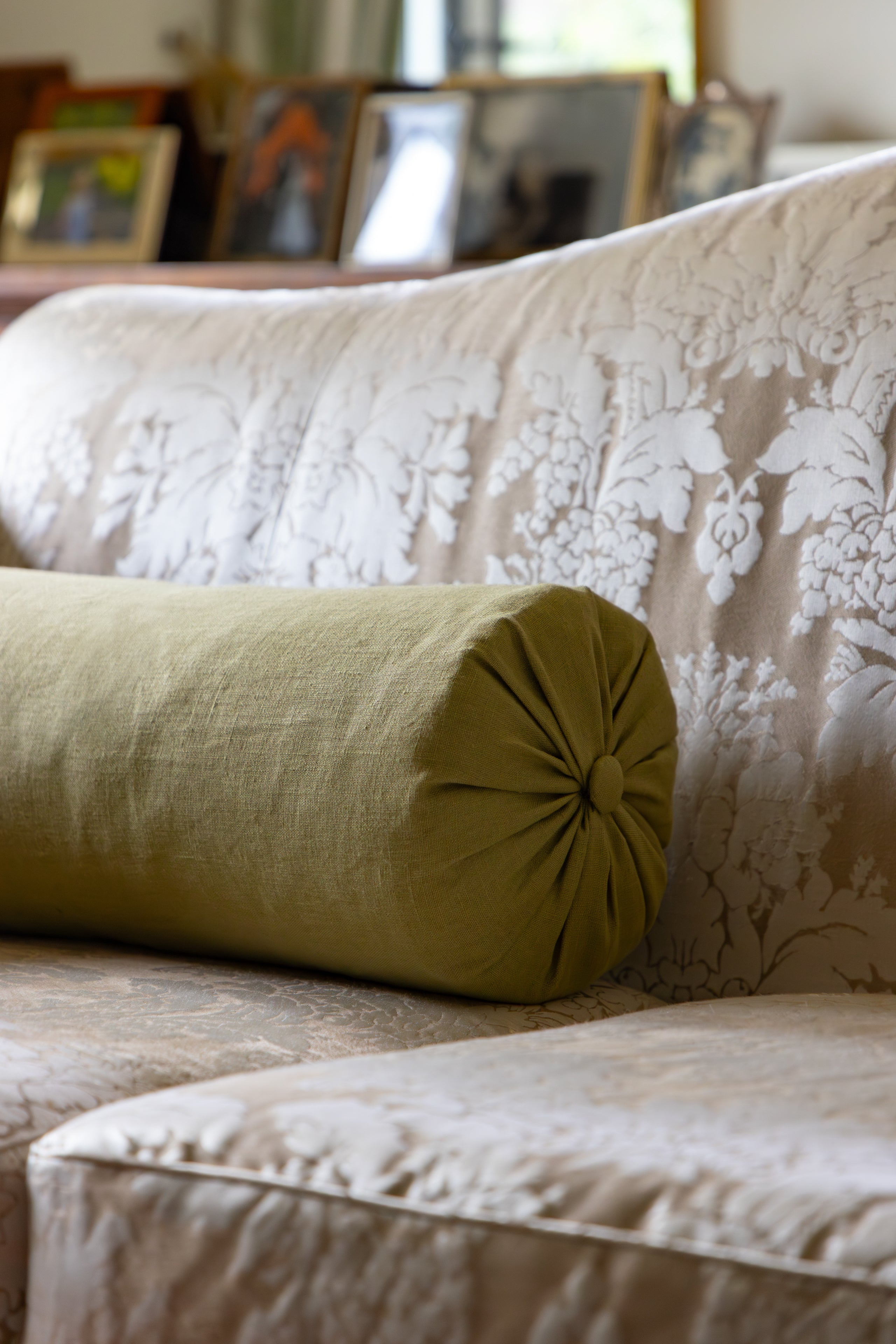 Green cylindrical pillow on a beige floral-patterned sofa