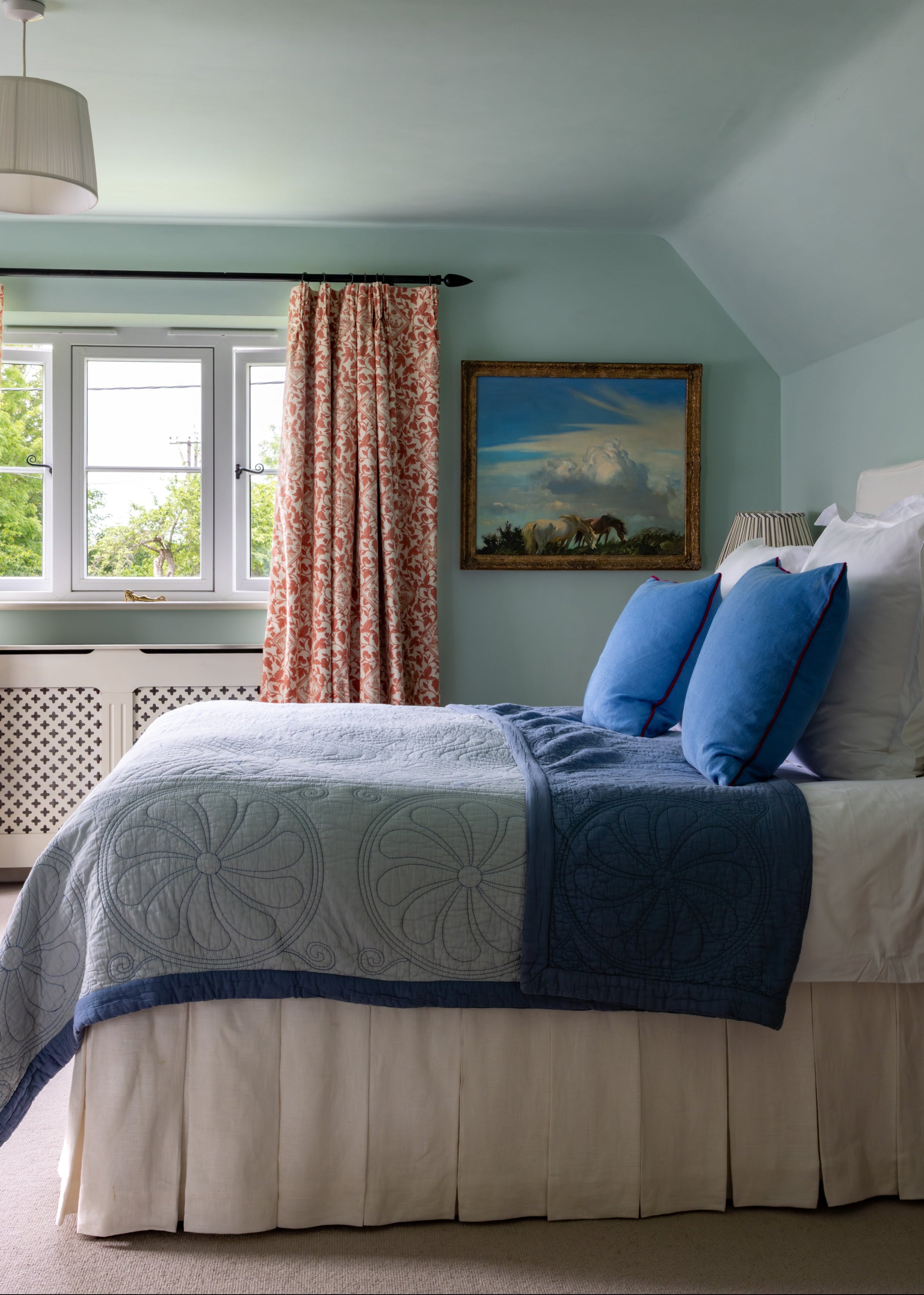 Bedroom with a bed featuring blue and white bedding, a window with pink curtains, and a painting on the wall.