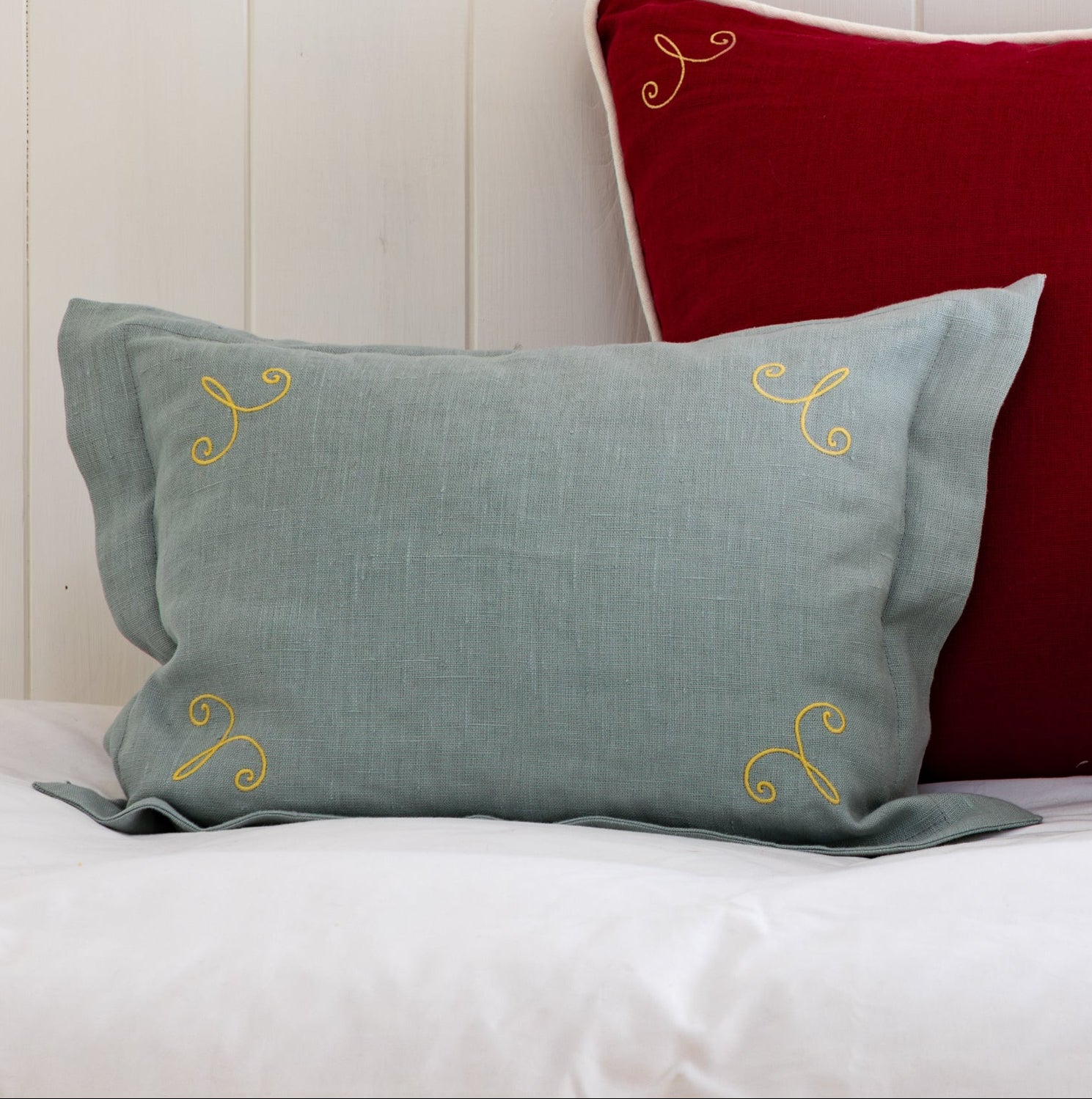 Three decorative pillows in red, gray, and green on a white surface with a wooden panel background.