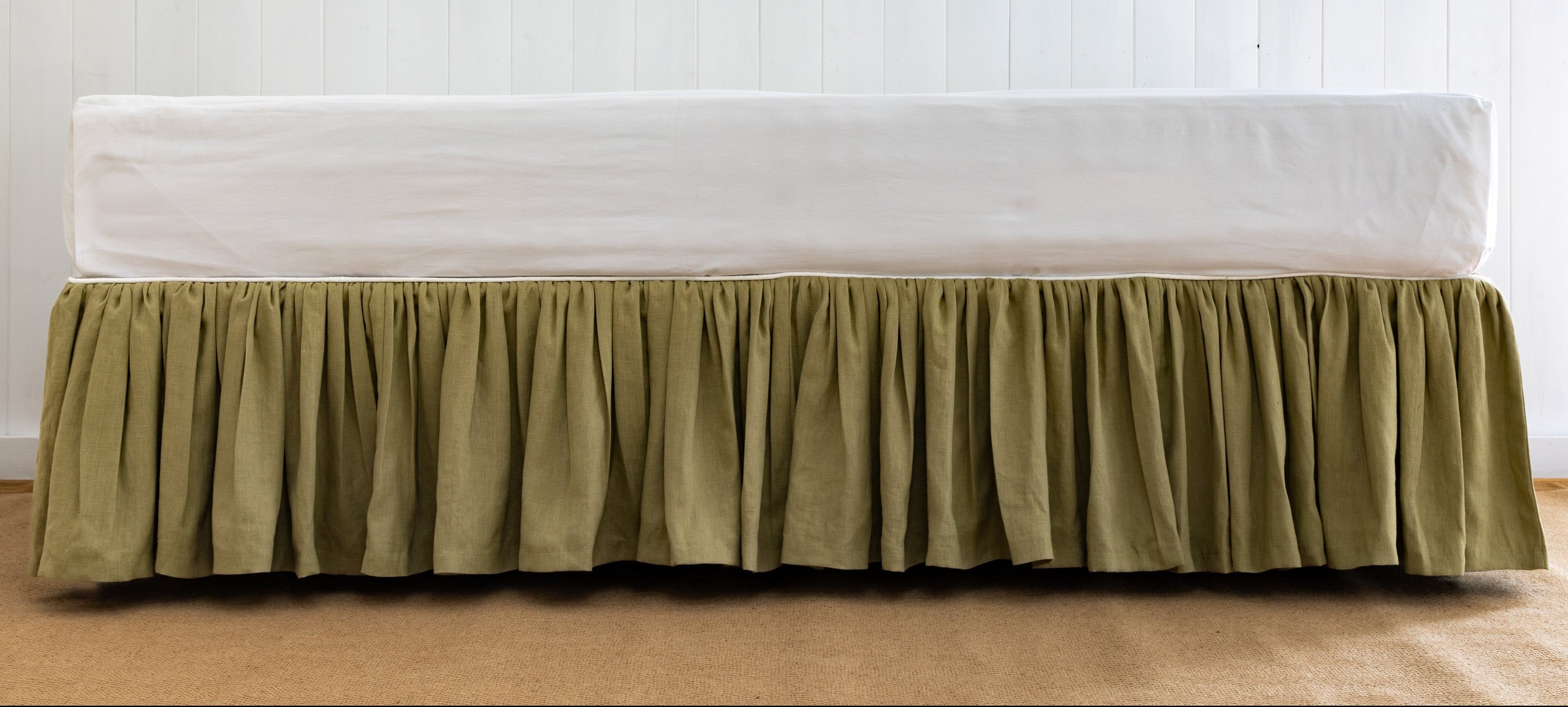 Bed with a green skirt and white mattress against a white wall.