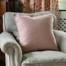 Pink pillow on a gray armchair with floral curtains and a vase in the background