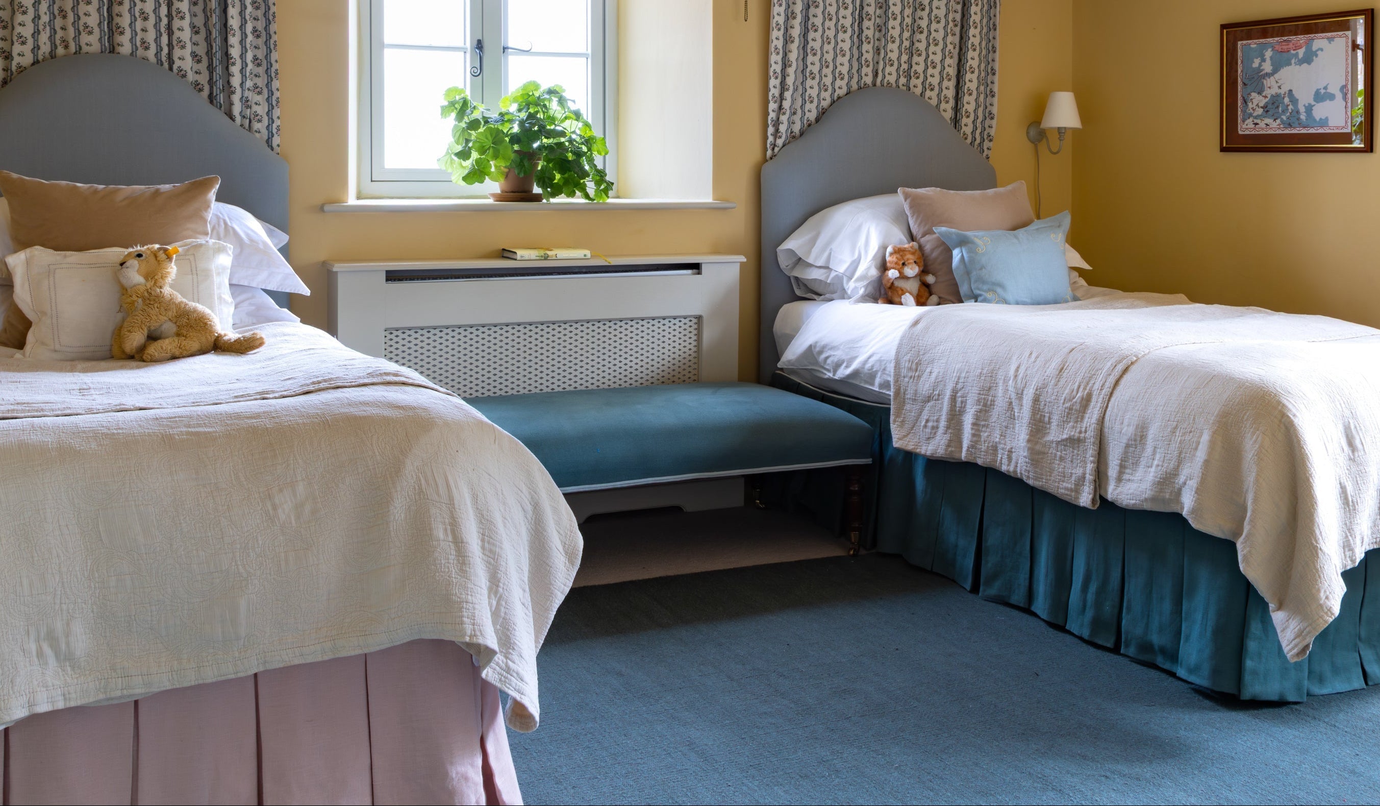 Two beds in a bedroom with yellow walls, a window, and decorative items. Bed Valances in Pink and Teal. Children's twin bedroom. 