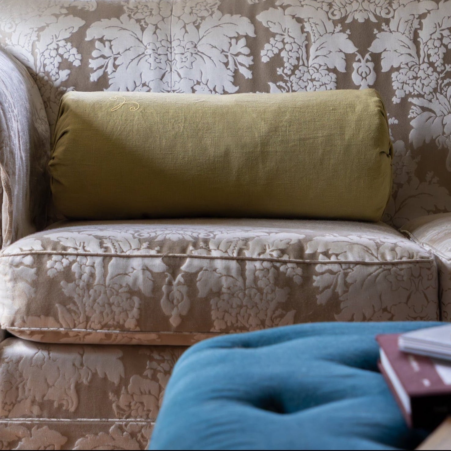 Living room with floral-patterned sofa, green pillow, and window with striped valance. Bolster cushion for bed or sofa