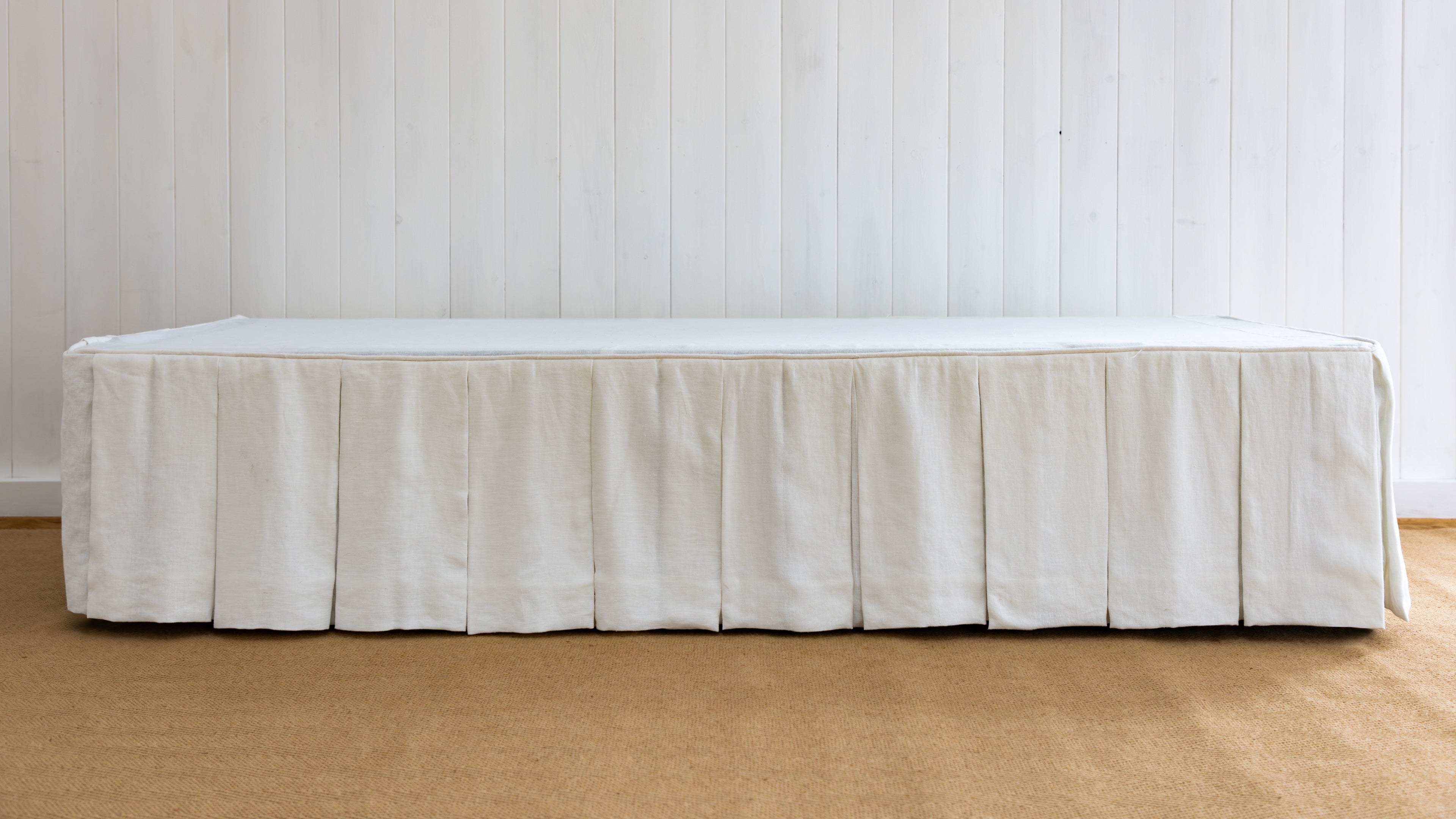 White bed skirt on a bed against a white paneled wall.