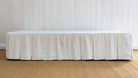 White bed skirt on a bed against a white paneled wall.
