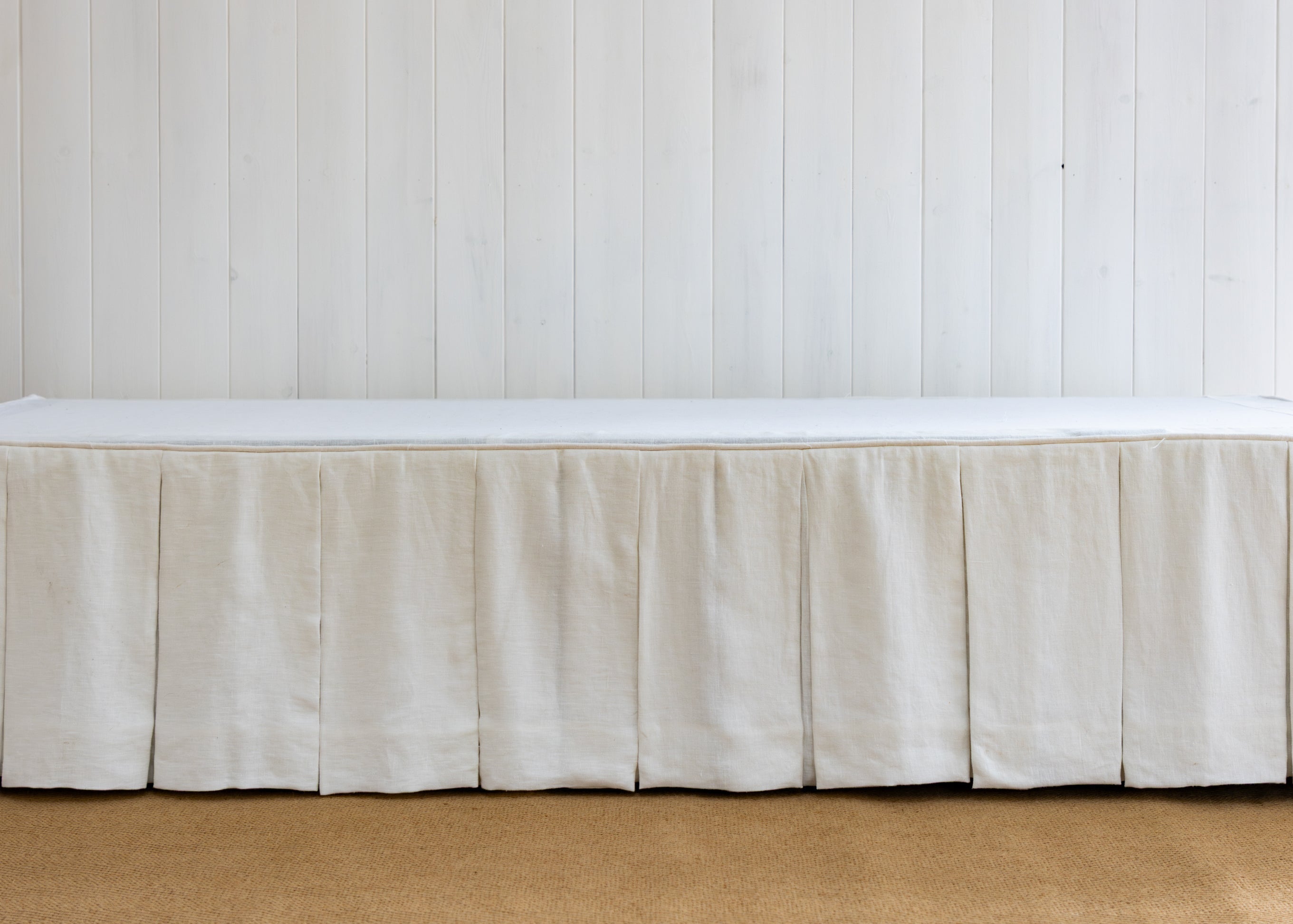 White bed skirt on a bed against a white paneled wall.