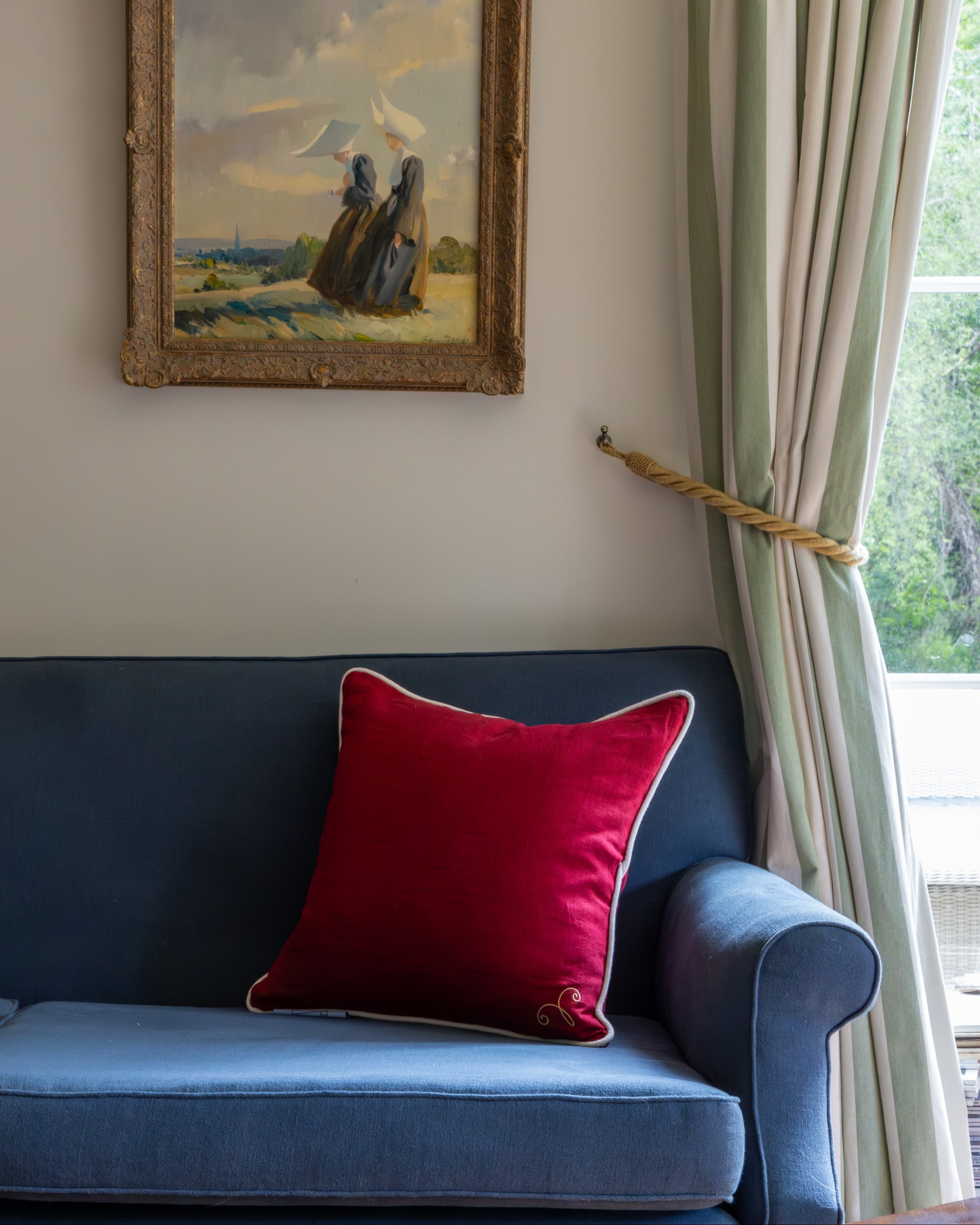 Blue sofa with a red pillow, framed painting on the wall, and green curtains.